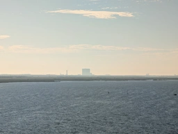 from the bridge, a large blocky building. to the right of that, poking just above a smaller, flatter building, is the rocket, straddled by two supports